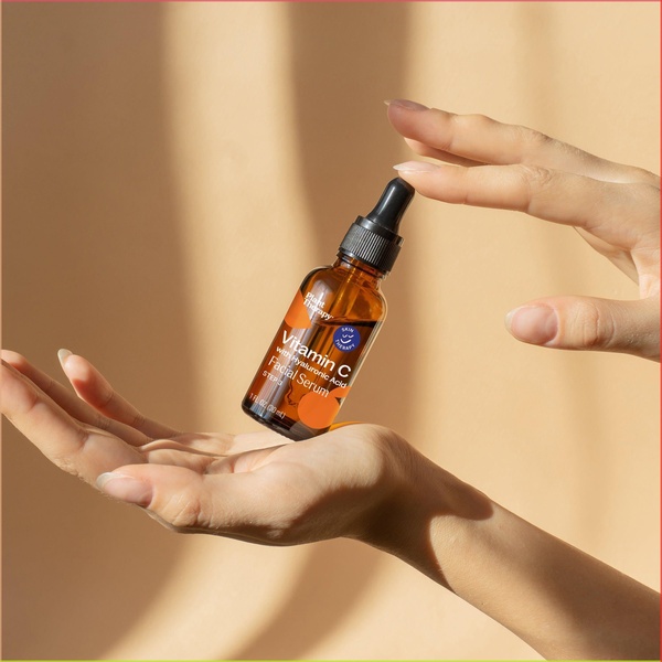 A clean, minimalist product hero shot of a facial serum bottle held between hands against a warm, neutral background to emphasize natural ingredients.